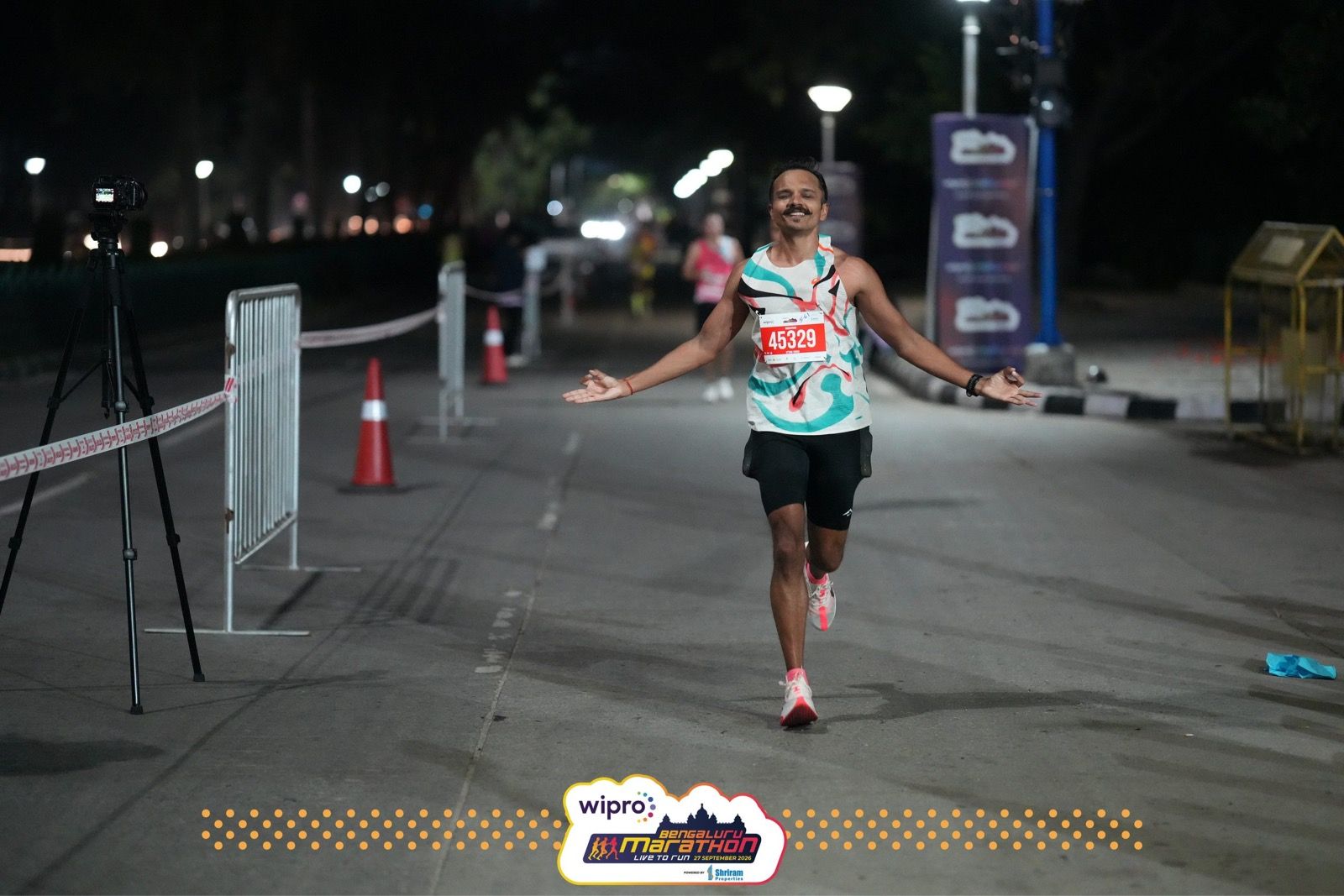 Uttam runs toward the camera with his arms spread wide on a dark, empty stretch of road lit by streetlights.