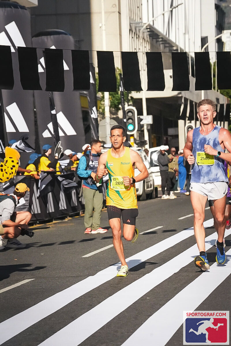 Vijay striding under a banner of Adidas branding in the closing stages of the race, focused, bib 2692 visible.