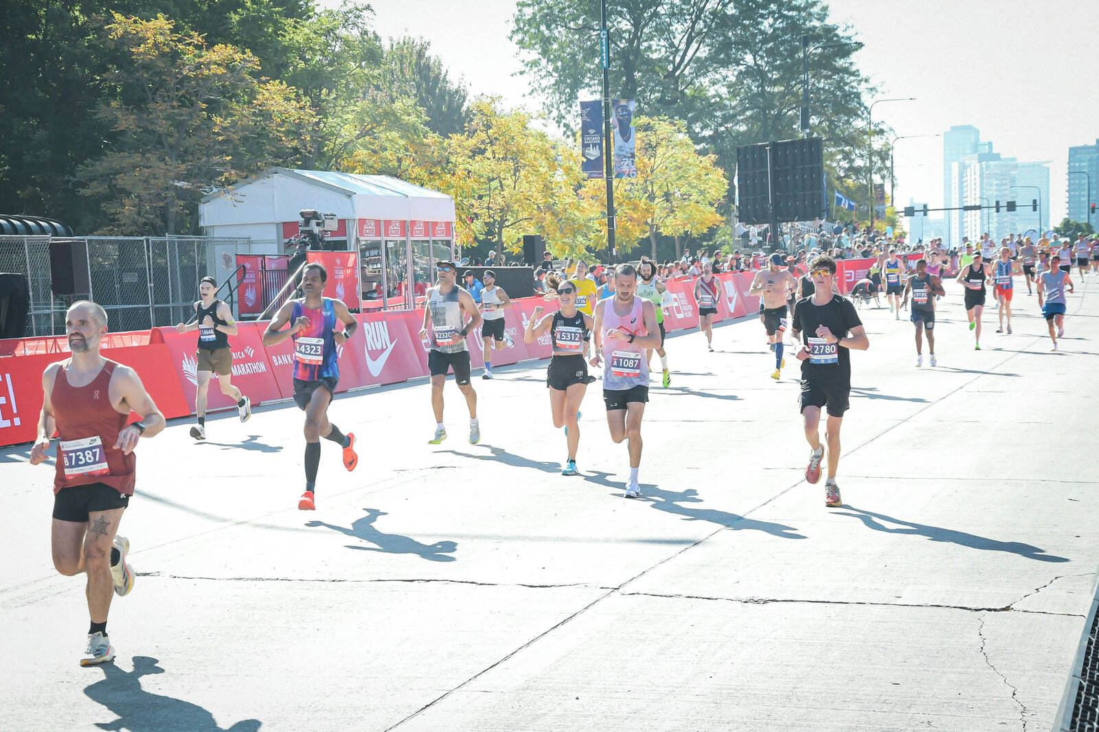 Murali Gaddam, bib B4323, runs along a barriered Chicago boulevard with other runners, trees and the city skyline behind him.