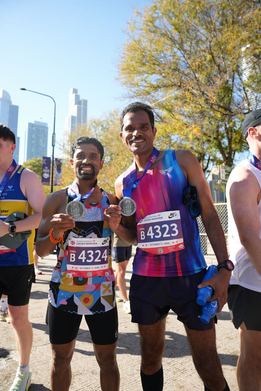 Murali Gaddam and Vikram stand together after the race, each holding up a Chicago Marathon medal.