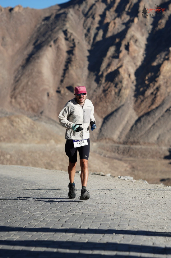 Oliver running on a cobbled road with a steep, bare mountain face behind him, wearing the windcheater and gloves.