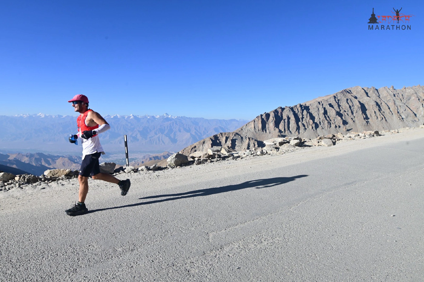 Oliver running away from the camera on a gravel road in the red vest, heading down towards the valley, with snow peaks on the horizon.