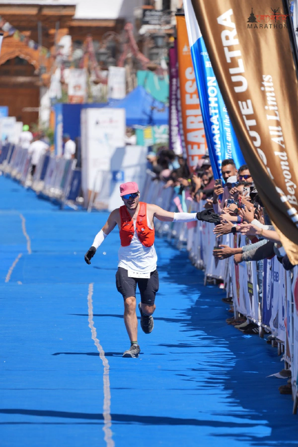 Oliver running down the blue finish carpet with his arms out, the crowd reaching over the barriers on the right and a 'Beyond All Limits' banner overhead.