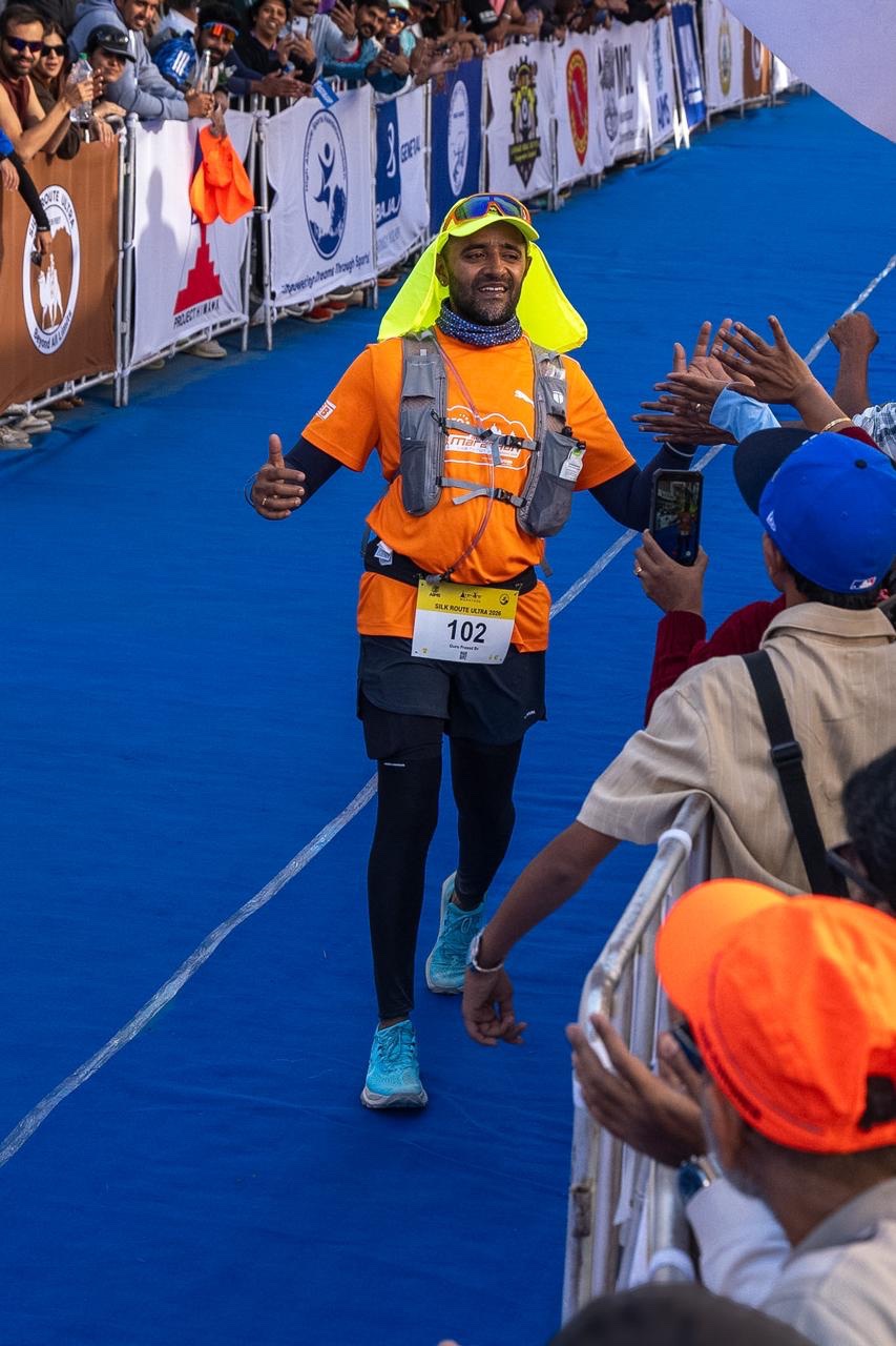 Guru, bib 102, in an orange T-shirt, black tights and a yellow sun-protection cap, high-fives spectators along the blue carpet in Leh.